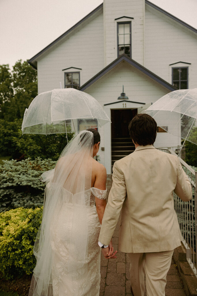 Bride and Groom with umbrellas walking into the Bayfield Town Hall on their wedding day.

